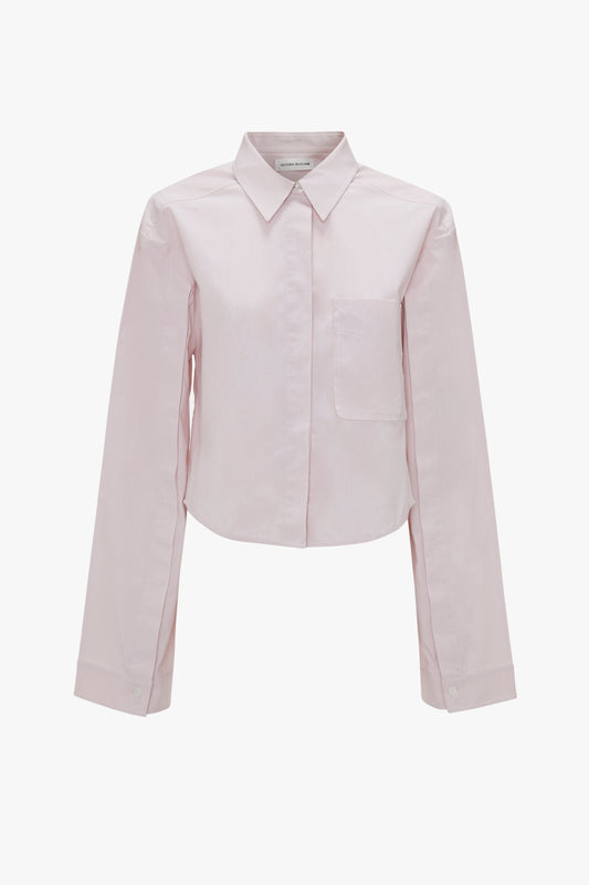 A Victoria Beckham Button Detail Cropped Shirt In Rose Quartz with a collar, pleated back, and a front chest pocket, displayed against a white background.