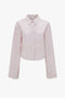 A Victoria Beckham Button Detail Cropped Shirt In Rose Quartz with a collar, pleated back, and a front chest pocket, displayed against a white background.