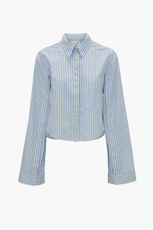 A long-sleeved, collared shirt with vertical blue and white stripes, featuring a cropped fit and button-down front. This Button Detail Cropped Shirt In Chamomile Blue Stripe exudes a feminine silhouette that would complement any wardrobe inspired by Victoria Beckham's chic style.
