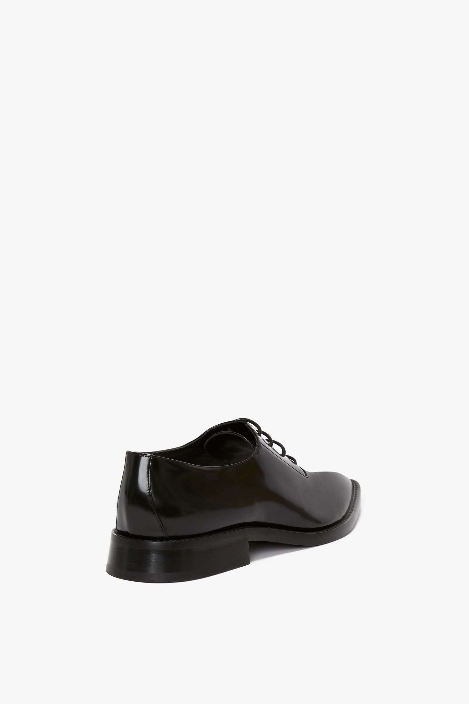 A single black leather dress shoe with a shiny surface and directional pointy toe, viewed from the back at an angle on a white background. This is the Pointy Toe Flat Lace Up In Black Brushed Leather by Victoria Beckham.