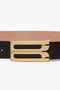 Close-up of an Exclusive Jumbo Frame Belt in black leather from Victoria Beckham, featuring a gold-toned, minimalist buckle that highlights the texture and details of the metal and leather surfaces.