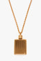 A gold rectangular pendant with a ridged pattern hangs from a gold brushed brass chain, reminiscent of an Exclusive Perfume Bottle Necklace In Brushed Gold by Victoria Beckham.