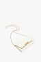 An Exclusive Wallet On Chain In White Leather by Victoria Beckham with a gold chain strap and gold clasp lies against a white background.