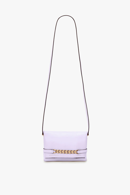 A Victoria Beckham Exclusive Mini Chain Pouch Bag With Long Strap In Lilac Leather featuring a long black strap, gold chain detailing on the front flap, and a versatile detachable strap.