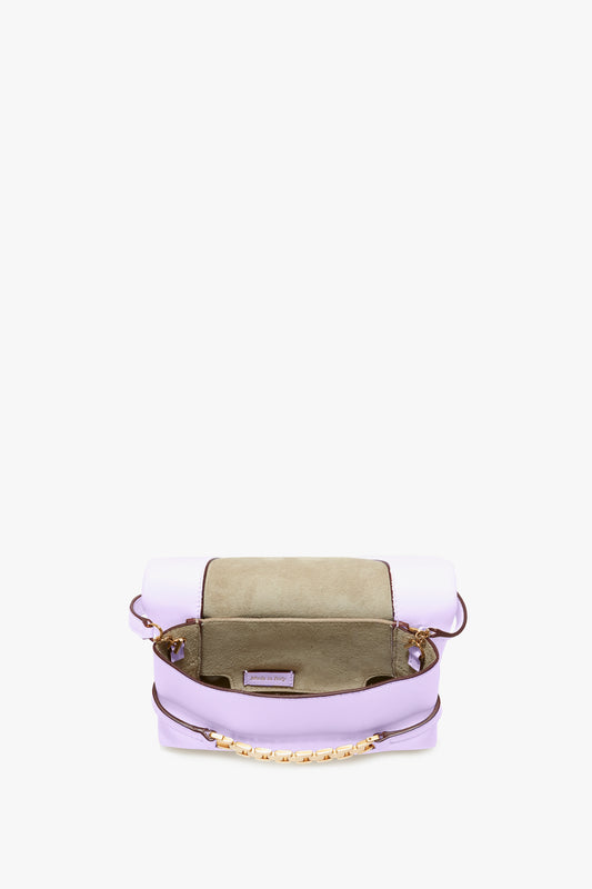 A Victoria Beckham Exclusive Mini Chain Pouch Bag With Long Strap In Lilac Leather with an open flap reveals its interior. The bag is lilac with an olive green section under the flap and a gold chain handle.