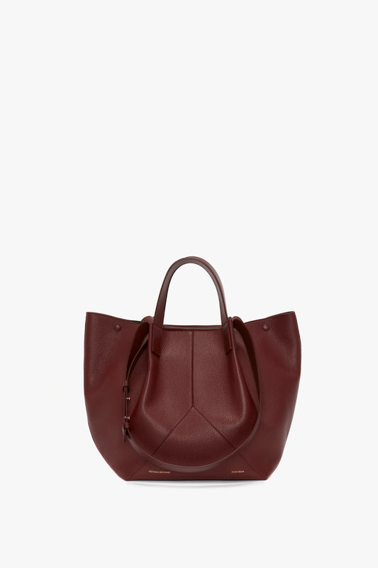 A dark red W11 Medium Tote Bag In Burgundy Leather by Victoria Beckham with two handles and a textured surface, perfect for versatile styling, displayed against a plain white background.