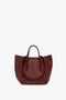 A dark red W11 Medium Tote Bag In Burgundy Leather by Victoria Beckham with two handles and a textured surface, perfect for versatile styling, displayed against a plain white background.