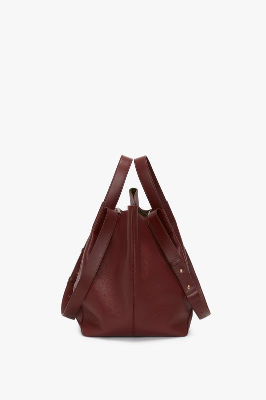 A dark red, grained leather W11 Medium Tote Bag In Burgundy Leather by Victoria Beckham with a drawstring closure and adjustable straps, seen from the back against a plain white background. Perfect for versatile styling.