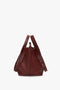 A dark red, grained leather W11 Medium Tote Bag In Burgundy Leather by Victoria Beckham with a drawstring closure and adjustable straps, seen from the back against a plain white background. Perfect for versatile styling.