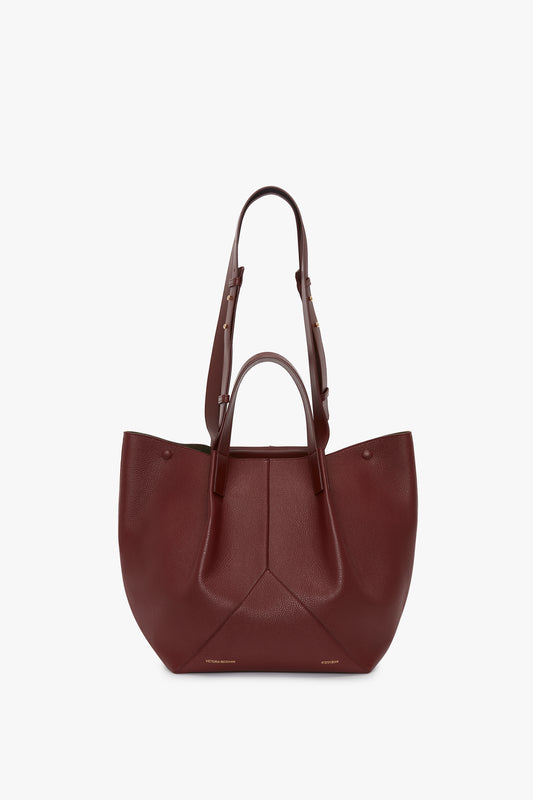 A large, stylish, dark red grained leather tote bag with both shoulder and hand straps, featuring a structured design and minimalistic stitching for versatile styling becomes the Victoria Beckham W11 Medium Tote Bag In Burgundy Leather.