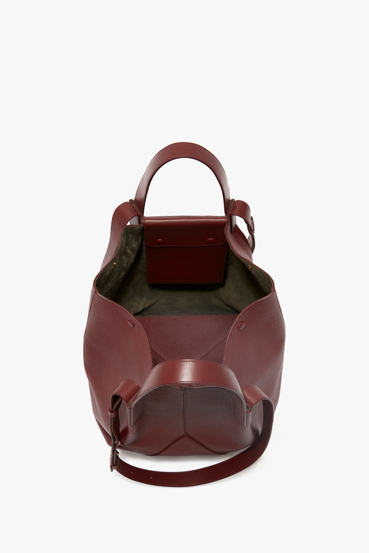 A W11 Medium Tote Bag In Burgundy Leather crafted from maroon grained leather, featuring an open top that reveals an empty main compartment and an internal pocket. The bag offers versatile styling with short handles and an adjustable shoulder strap by Victoria Beckham.