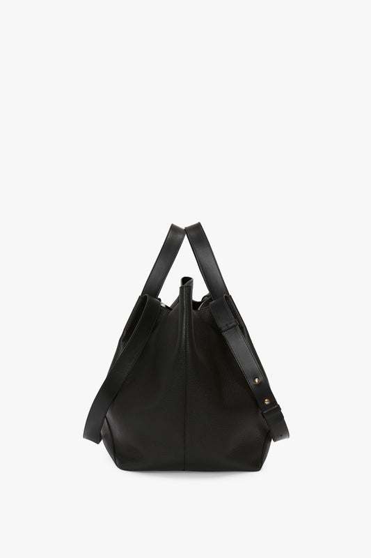 A W11 Medium Tote Bag In Black Leather with a slouchy, relaxed shape, featuring dual handles and a shoulder strap with gold-tone hardware. This medium tote reflects Victoria Beckham's signature style in premium leather goods.