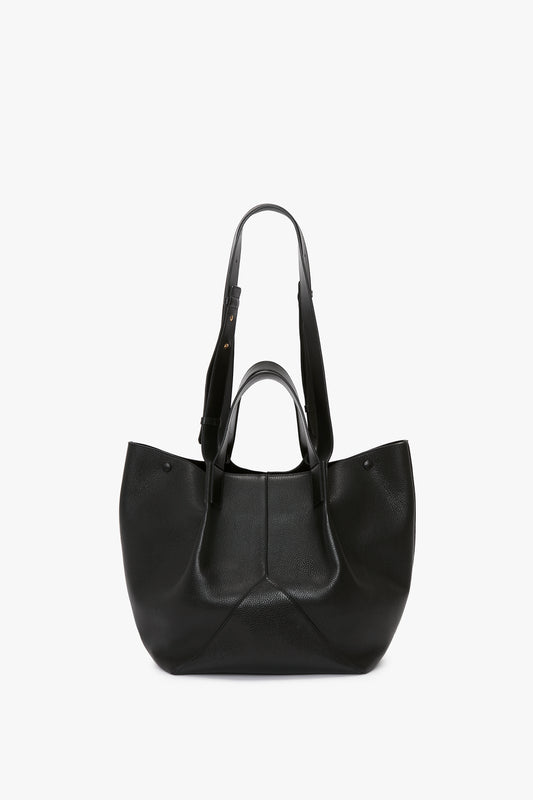 A W11 Medium Tote Bag In Black Leather with dual shoulder straps, an open top, and a textured surface, set against a plain white background. This Victoria Beckham creation showcases the elegance of premium leather goods.