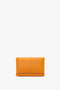 A rectangular bright mandarin leather clutch with clean lines and minimal detailing, paired with a Mini Chain Pouch Bag With Long Strap In Mandarin Leather from Victoria Beckham, is elegantly placed against a plain white background.