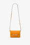 A bright Mini Chain Pouch Bag With Long Strap In Mandarin Leather by Victoria Beckham with a structured rectangular shape. It features a flap closure with metallic interlocking accents and a long, thin strap.