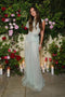 A woman in a Gathered Tulle Detail Floor-Length Dress In Jade by Victoria Beckham stands in front of a floral backdrop with pink and red roses, surrounded by lit candles.