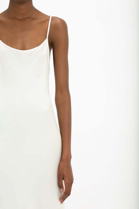 A close-up of a person wearing a Victoria Beckham Floor-Length Cami Dress In Ivory. The focus is on the torso and arms, evoking a sense of 90s fashion, with the background being white.