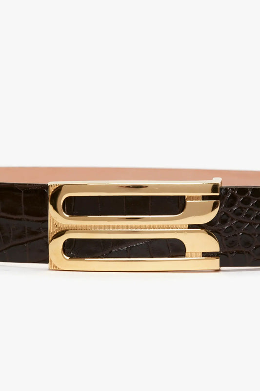 Close-up of a black croc-effect leather Jumbo Frame Belt In Chocolate Croc-Effect Leather by Victoria Beckham with a gold buckle featuring a sleek, rectangular design with smooth and textured details.