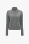 A Polo Neck Jumper In Grey Melange, crafted from luxurious lambswool, is shown against a white background. The jumper features a ribbed texture on the neck, cuffs, and hem, with an elegant Victoria Beckham monogram subtly detailed.