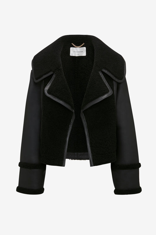 A luxurious **Shearling Jacket In Black** by **Victoria Beckham** with wide lapels and long sleeves boasts an aviator-style, set against a pristine white background.