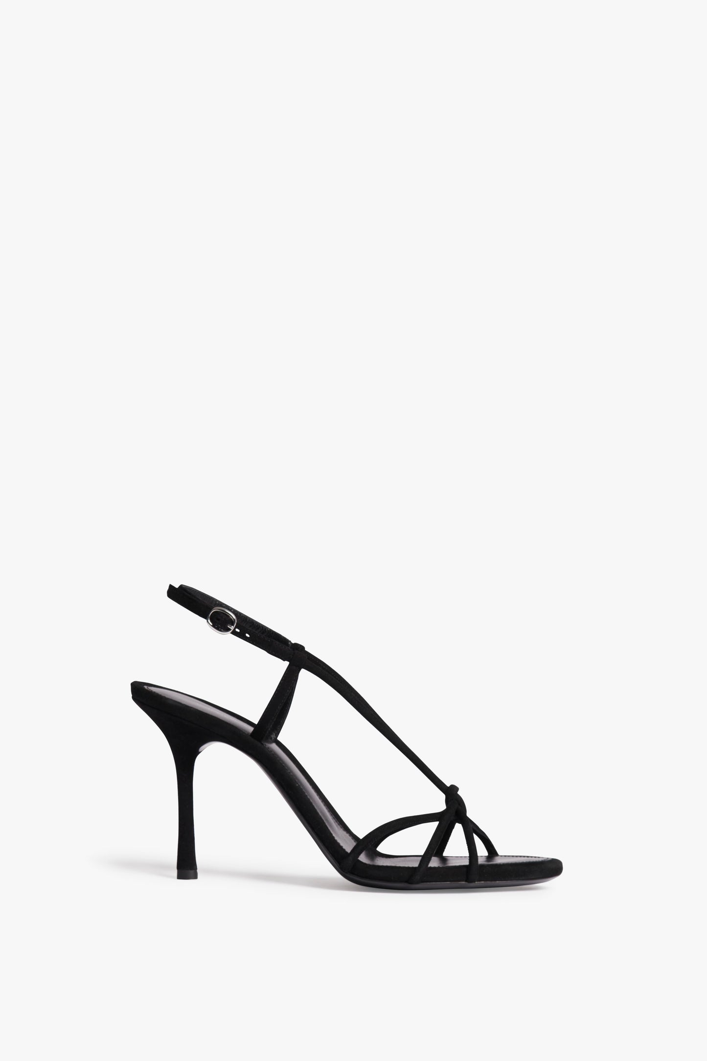 The Victoria Beckham Gaia Sandal in Black is a black suede high-heeled masterpiece with thin straps and an elegant ankle buckle, displayed on a plain white background.