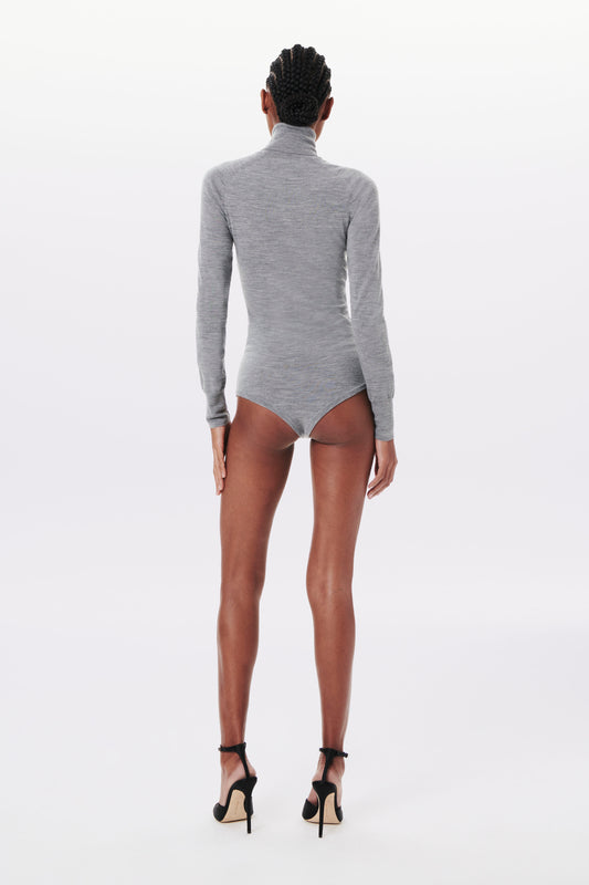 Person with braided hair is standing and facing away, wearing a Victoria Beckham Poloneck Bodysuit in Grey Marl and black high heels, against a plain background.