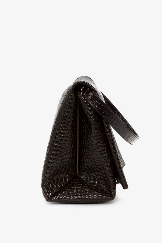 Side view of a Victoria Beckham Jumbo Chain Pouch Bag In Chocolate Croc-Effect Leather with a top handle flap, showcasing its versatile styling and luxurious touch.