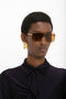 Person with short hair wearing Victoria Beckham Rectangular Visor Gold-Framed Sunglasses, geometric gold earrings, and a dark, collared shirt.