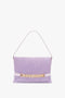 A Victoria Beckham Chain Pouch Bag with Strap in Lilac Suede, designed as a chic fold-over pouch bag, features a gold chain detail on the front and a single shoulder strap.