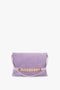 A **Chain Pouch Bag with Strap in Lilac Suede** from **Victoria Beckham**, crafted from Italian leather, featuring a gold chain detail, a matching shoulder strap, and a flap closure, is displayed on a white background.