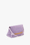 Image of a Victoria Beckham Chain Pouch Bag with Strap in Lilac Suede featuring a flap closure and gold chain detail, with a slim strap.