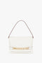 A Victoria Beckham Chain Pouch Bag with Strap In White Leather, crafted from luxurious Nappa leather, featuring a single strap and a fold-over flap with a gold geometric accent. This elegant piece also includes a detachable strap for added versatility.