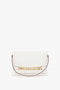 A white rectangular Chain Pouch Bag with Strap In White Leather by Victoria Beckham with a gold chain detail on the front and a thin maroon detachable strap.