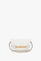 A Mini Chain Pouch Bag In White Leather, crafted from luxurious Nappa leather, adorned with gold accents on the front, and featuring a thin maroon detachable strap. Branded with "Victoria Beckham" and "TRIPON 1997" on the bottom, this mini pouch embodies elegance.