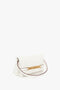 A Mini Chain Pouch Bag In White Leather with a gold chain detail, a brown shoulder strap, and embossed with "Victoria Beckham," featuring a mini pouch and a detachable strap for versatile styling.