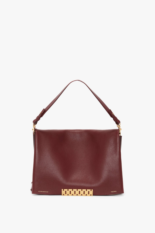 A Jumbo Chain Pouch Bag In Bordeaux crafted from grained leather by Victoria Beckham, featuring a gold clasp and a single shoulder strap against a white background. The handbag also comes with a detachable strap for versatility and style.