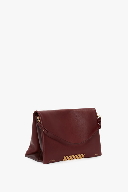A Victoria Beckham Jumbo Chain Pouch Bag In Bordeaux with a fold-over flap, gold-tone hardware accents, and a detachable shoulder strap.