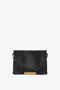 A Victoria Beckham Jumbo Chain Pouch Bag In Black Leather, featuring a gold chain detail on the front flap and a shoulder strap.