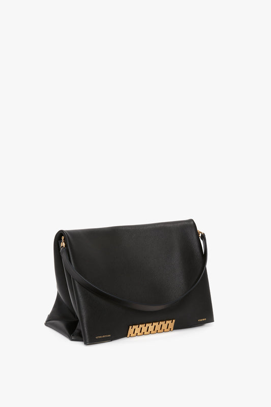 A black Nappa leather handbag with a flap closure, gold hardware, and a shoulder strap, reminiscent of the Victoria Beckham Jumbo Chain Pouch Bag In Black Leather, set against a plain white background.