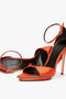 Two Victoria Beckham Pointy Toe Stiletto Sandals in Orange Satin, featuring a leg-lengthening platform sole and elegant ankle straps, one upright and one laying on its side, with an open-toe design made from luxurious silk-satin blend fabric against a white background.