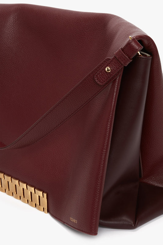 A close-up of a Victoria Beckham Jumbo Chain Pouch Bag In Bordeaux with a gold metal clasp detail on the lower edge, and a detachable strap for versatile styling.