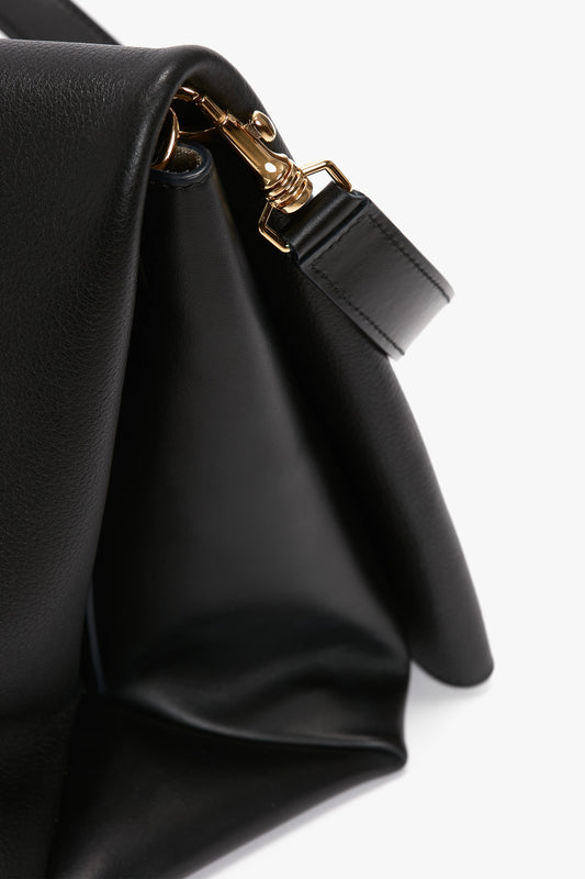 Close-up of a black Nappa leather Jumbo Chain Pouch Bag In Black Leather by Victoria Beckham with a gold buckle and clasp, showing detailed texture and stitching of the material.