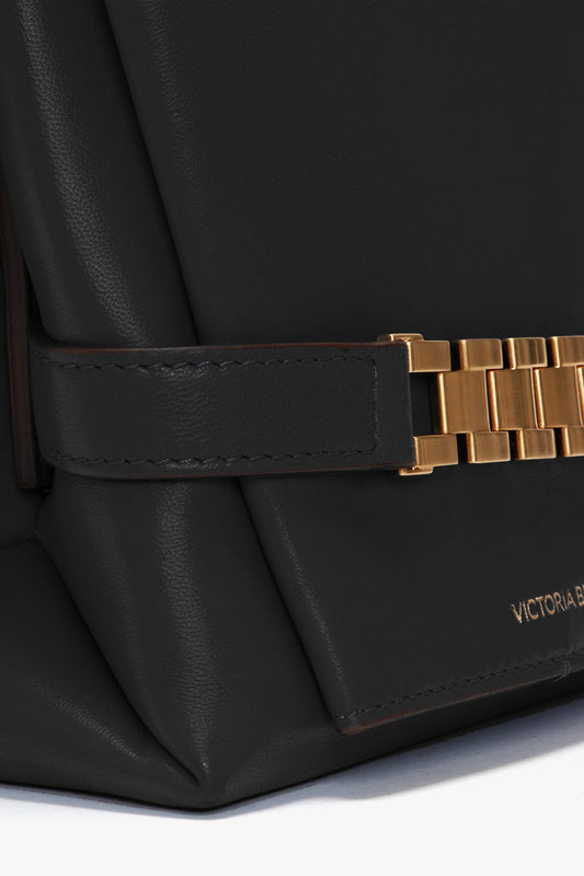 Close-up of a black Nappa leather Chain Pouch Bag with Strap In Black Leather, featuring gold-tone chain hardware and a subtle logo that reads "Victoria Beckham".