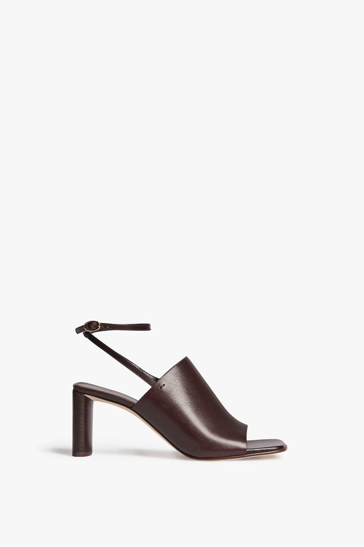 The Alina Sandal in dark brown. Square open-toe shape with an oval heel and minimal cross-over leather strap and adjustable ankle strap. Versatile mid-height, thick-heeled shoes from Victoria Beckham Footwear.