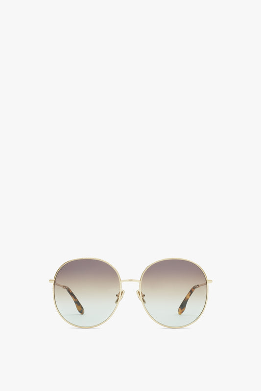 Victoria Beckham Hammered Round Sunglasses In Gold Brown Aqua with thin gold frames and gradient tinted lenses displayed against a white background. The temples have a tortoiseshell pattern, and the adjustable nose pads ensure a comfortable fit.