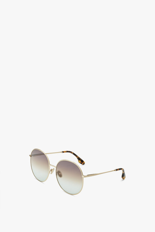 A pair of Hammered Round Sunglasses In Gold Brown Aqua by Victoria Beckham with thin gold frames, tortoiseshell temple tips, and adjustable nose pads, set against a white background.