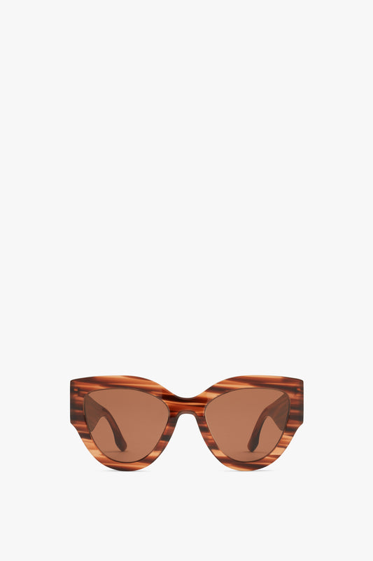 Pair of Oversized Cat Eye Sunglasses In Striped Brown by Victoria Beckham with a striped pattern on the frame and tinted lenses, crafted from glossy acetate, against a plain white background.