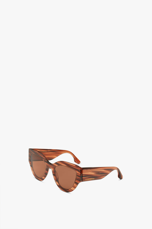 Pair of Victoria Beckham Oversized Cat Eye Sunglasses In Striped Brown with tinted lenses, crafted from glossy acetate, displayed against a plain white background.