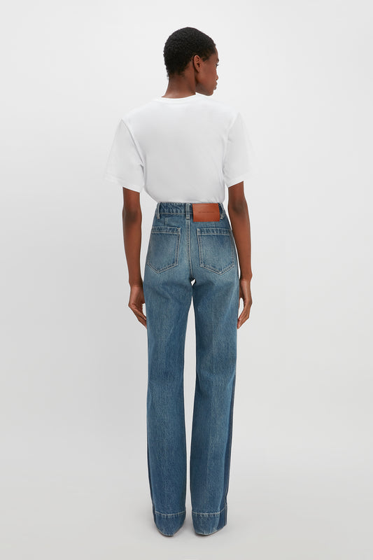 Individual with short hair, wearing a white t-shirt and high-waisted blue Alina High Waisted Jean In Shadow Wash by Victoria Beckham, standing with their back facing the camera against a plain white background.