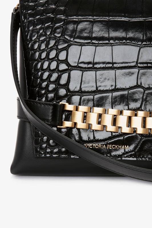 Close-up of a Chain Pouch Bag With Strap In Black Croc-Effect Leather with a gold chain detail and "Victoria Beckham" embossed at the bottom.